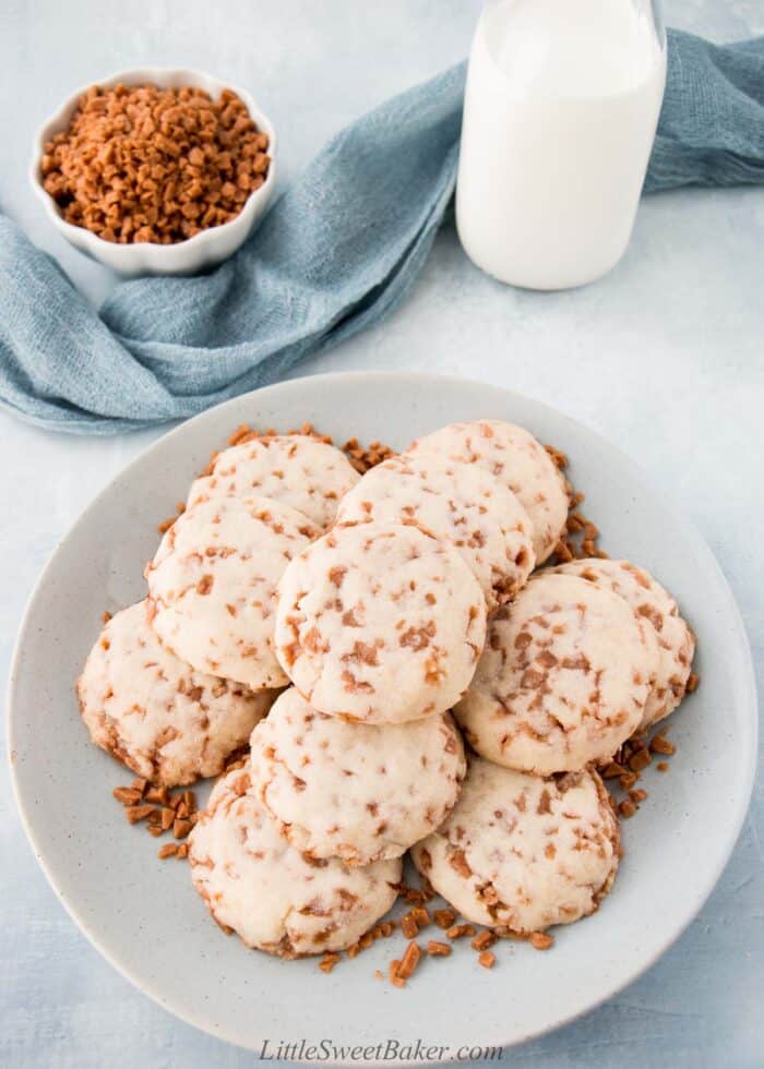 A plate of toffee shortbread cookies with a glass of milk and small bowl of Skor bits.