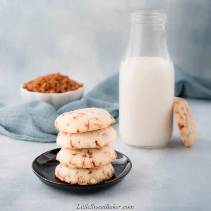 A stack of Skor bit shortbread cookies with one leaning on a tall glass of milk.