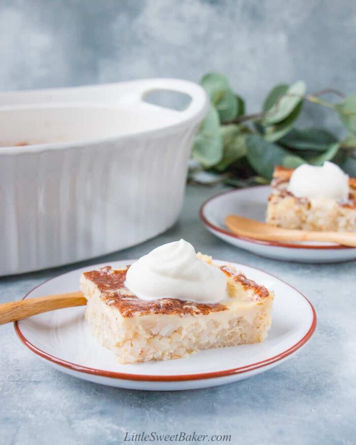 A slice of baked rice pudding topped with whipped cream on a light gray plate.