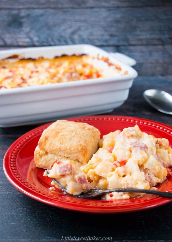 A plate of ham and potato casserole with a butter biscuit and fork.