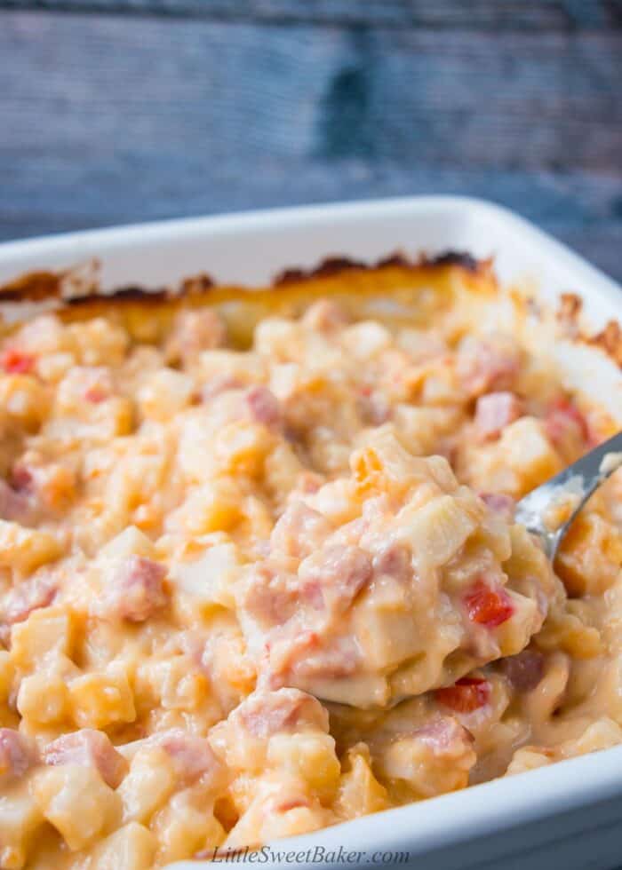 A dish of ham and potato casserole with a spoon being scooped out.