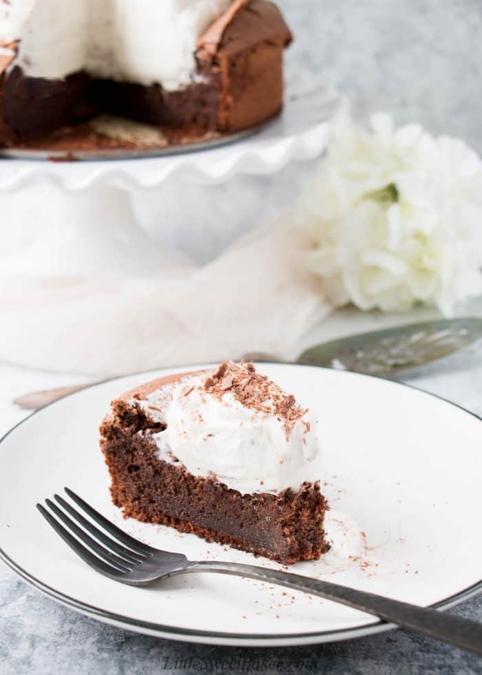 A slice of flourless chocolate torte topped with whipped cream and chocolate shavings.