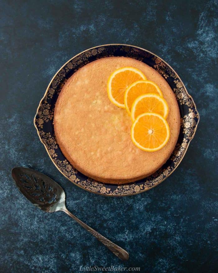 A flourless orange almond cake topped with orange slices on a navy blue and gold vintage plate.