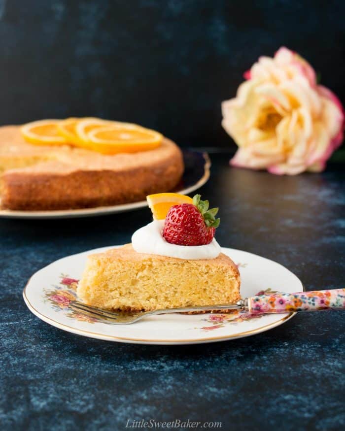 A slice of orange almond cake topped with whipped cream, strawberry and orange slice.