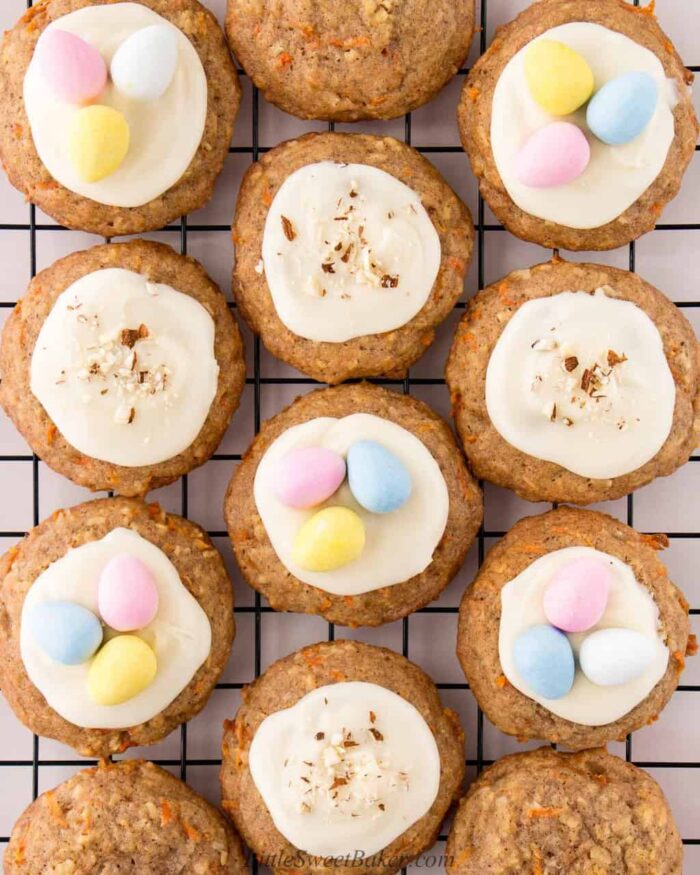 Carrot cake cookies topped with cream cheese, mini eggs and chopped nuts on a cooling rack.