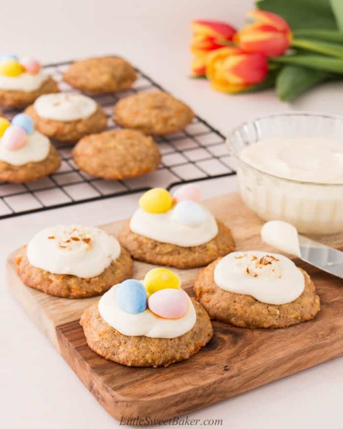 Carrot cake cookies topped with cream cheese frosting on a wooden board.