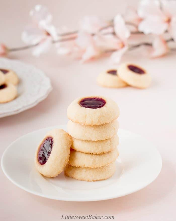 Six raspberry thumbprint cookies on a small white plate.