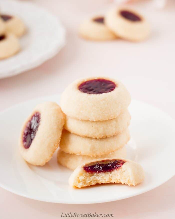 Raspberry thumbprint cookies on a small white plate with a bite taken out of one of them.