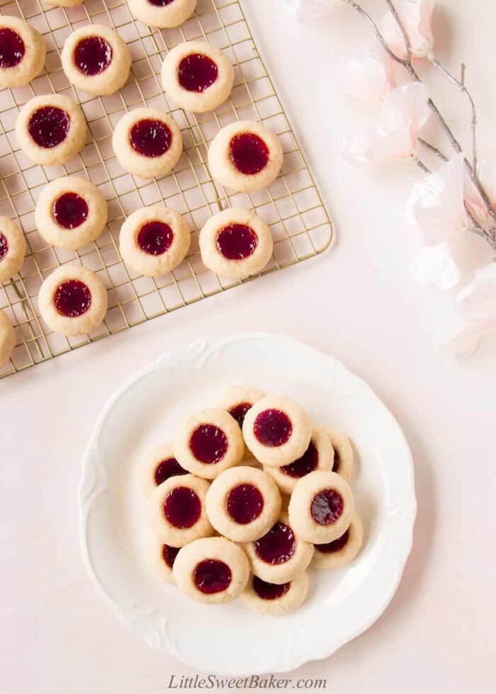 Raspberry thumbprint cookies on a cooling rack and on a white serving plate.