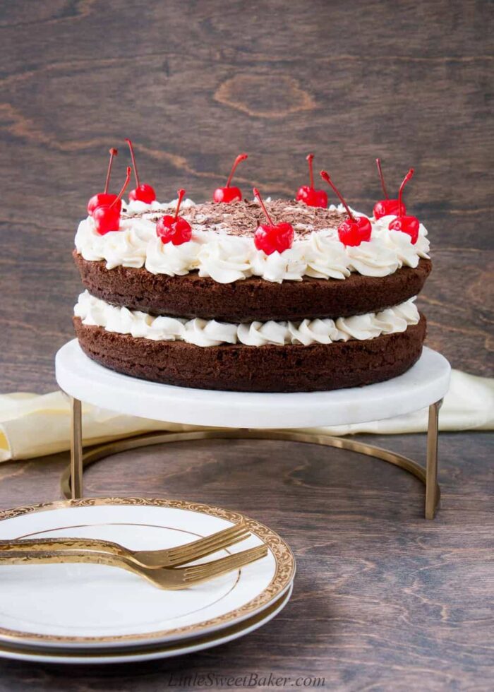 A whole black forest cake on a marble and gold cake stand.