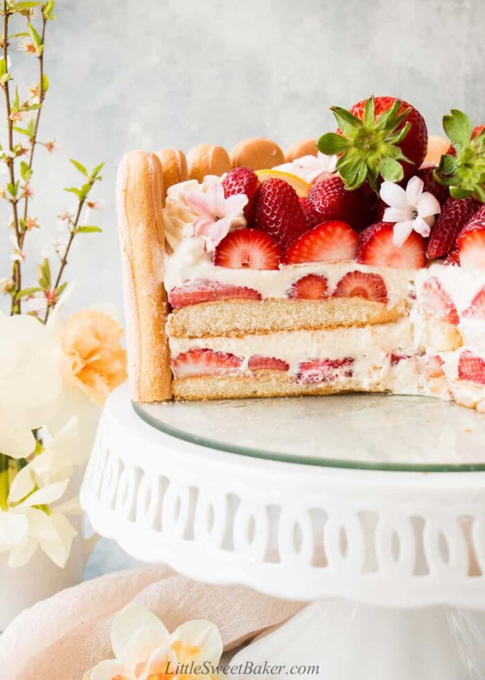 A cross section of a strawberry charlotte cake on a white cake stand.