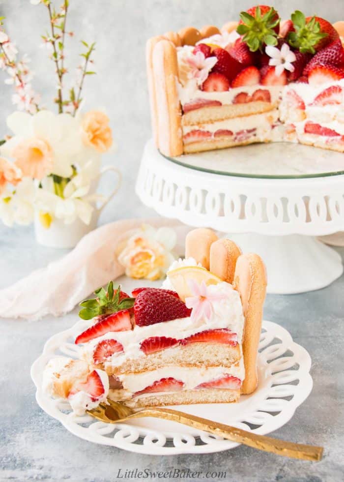 A slice of strawberry charlotte cake on a white laced rimmed plate.