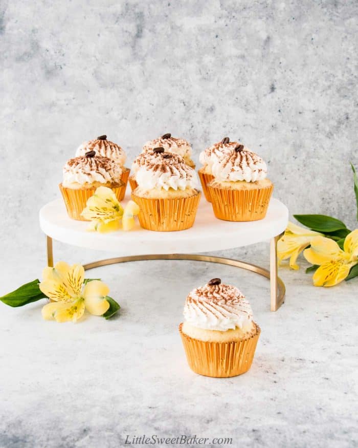 Tiramisu cupcakes on a gold and marble cake stand with yellow flowers.