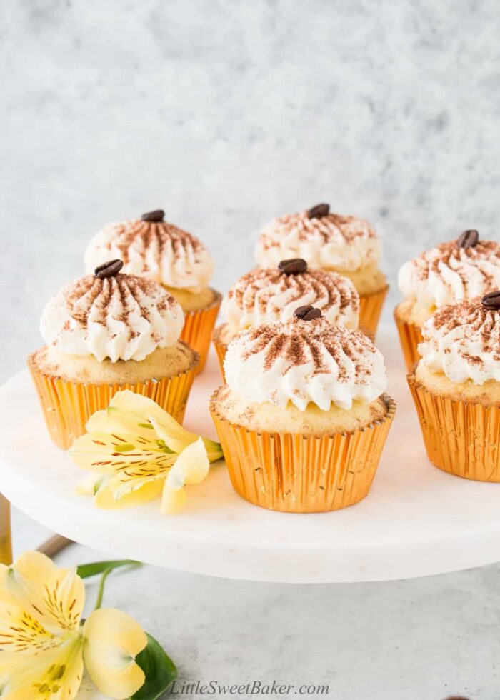 Tiramisu cupcakes on a white marble stand with yellow flowers.