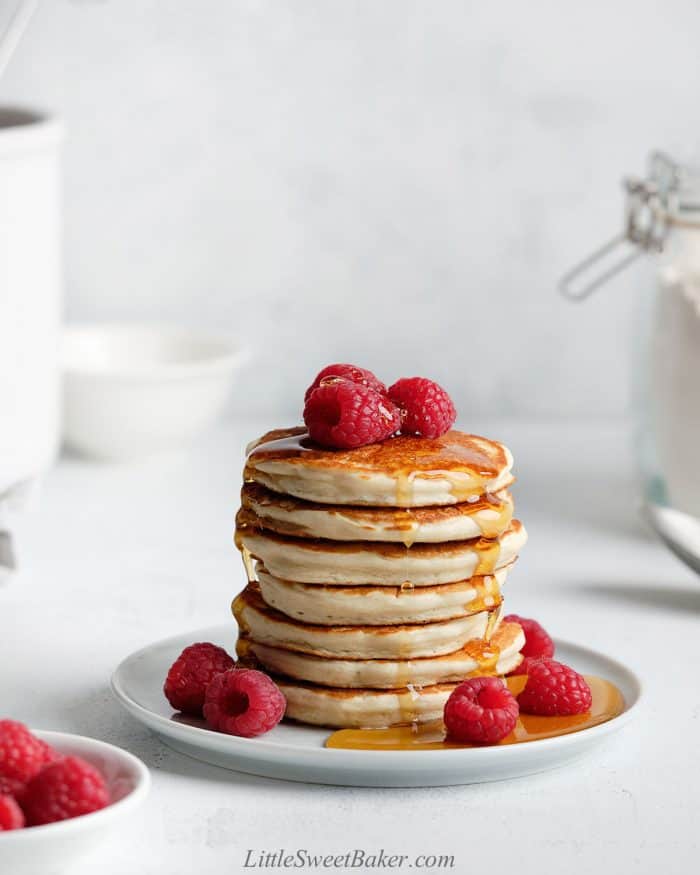 A stack of pancakes with maple syrup and raspberries.