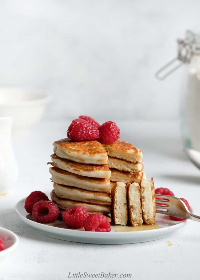 A stack of cut pancakes on a white plate with raspberries.