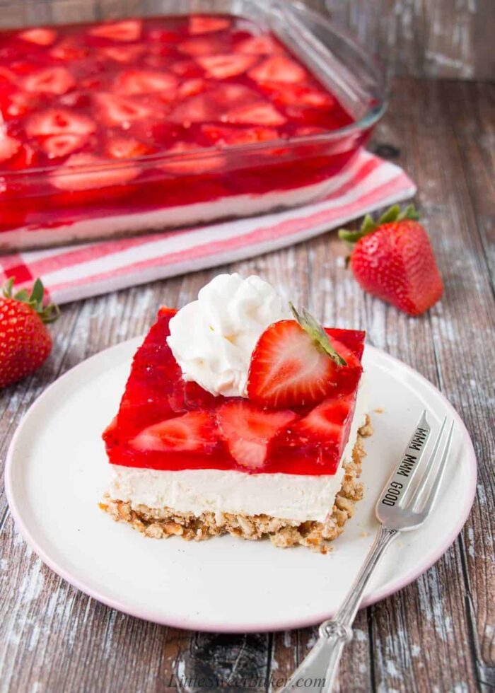 A slice of strawberry pretzel salad topped with whipped cream and half a strawberry.