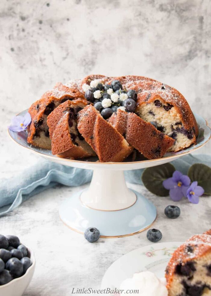 A blueberry bundt cake partially sliced on a blue cake plate.