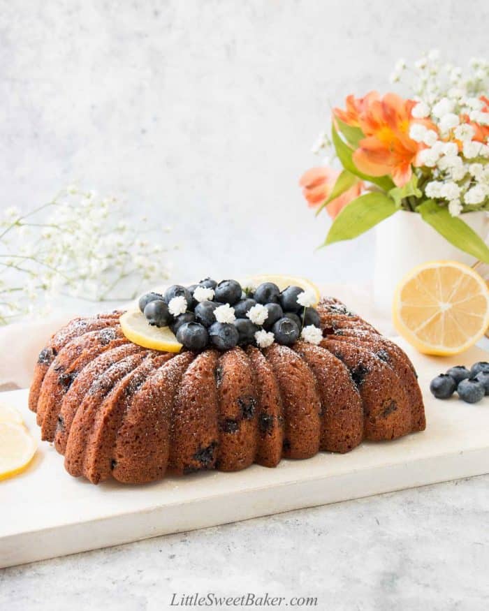 A loaf of lemon blueberry pound cake with blueberries, lemon, and white flowers on top.