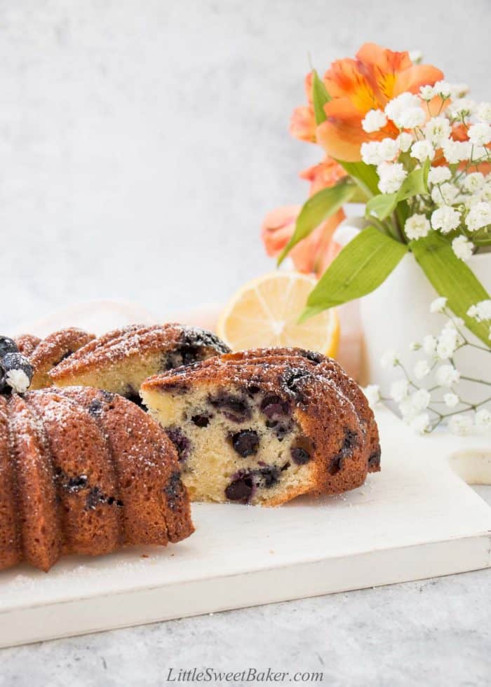 A slice of lemon blueberry pound cake pulled from a loaf on a white board.