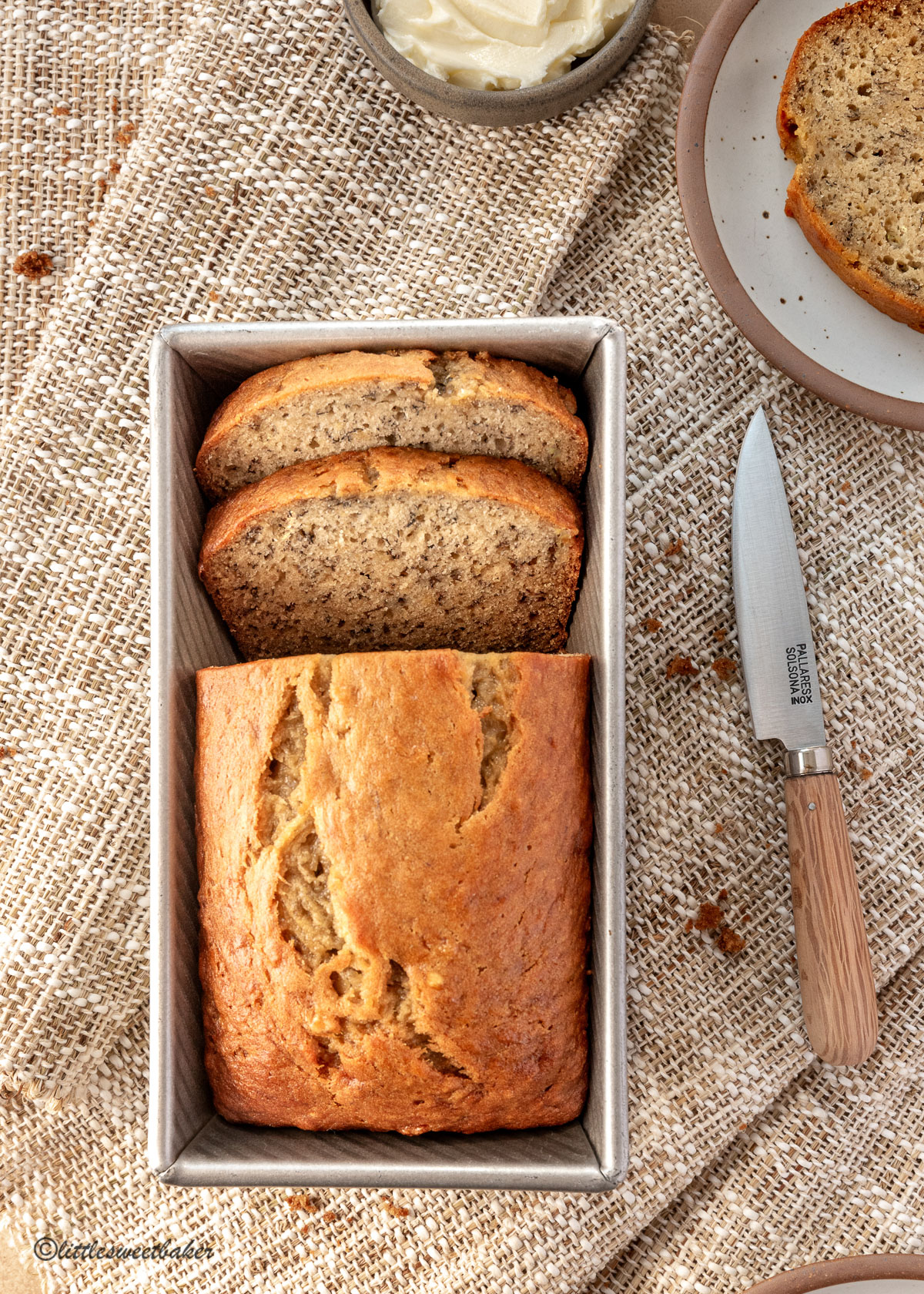 A loaf of banana bread in pan on brown canvas napkins.