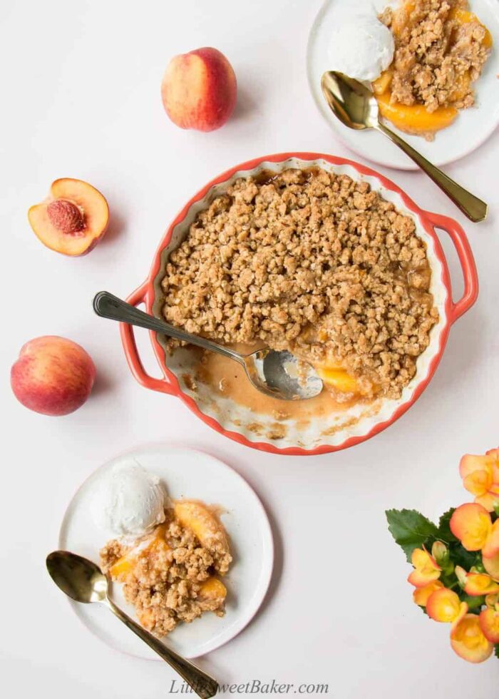 Peach crisp in a round ceramic dish with two servings on a plate a la mode.