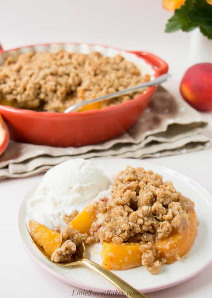 Peach crisp on a plate with a scoop of melty vanilla ice crean