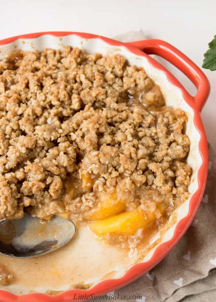 Peach crisp in a round serving dish with a few scoops missing.