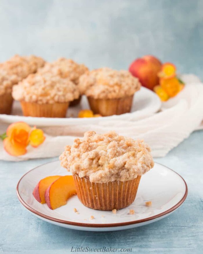 Peach muffin with crumb topping on a plate with two peach slices.