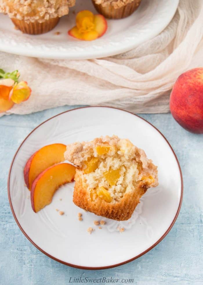 A peach crumb muffins with a big bite missing on a plate.