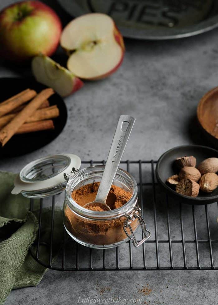 A jar of homemade apple pie spice mix with a measuring spoon inside on a black cooling rack.