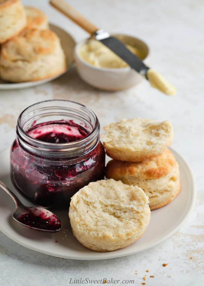 Two biscuits on a plate with a jar of jam.