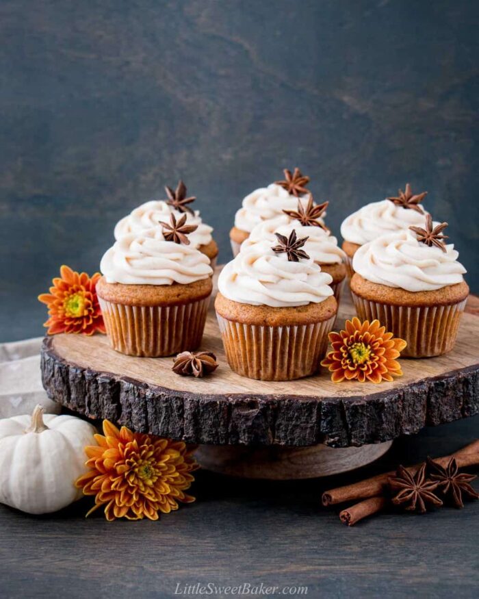 Pumpkin cupcakes with cream cheese frosting on a wooden cake stand.