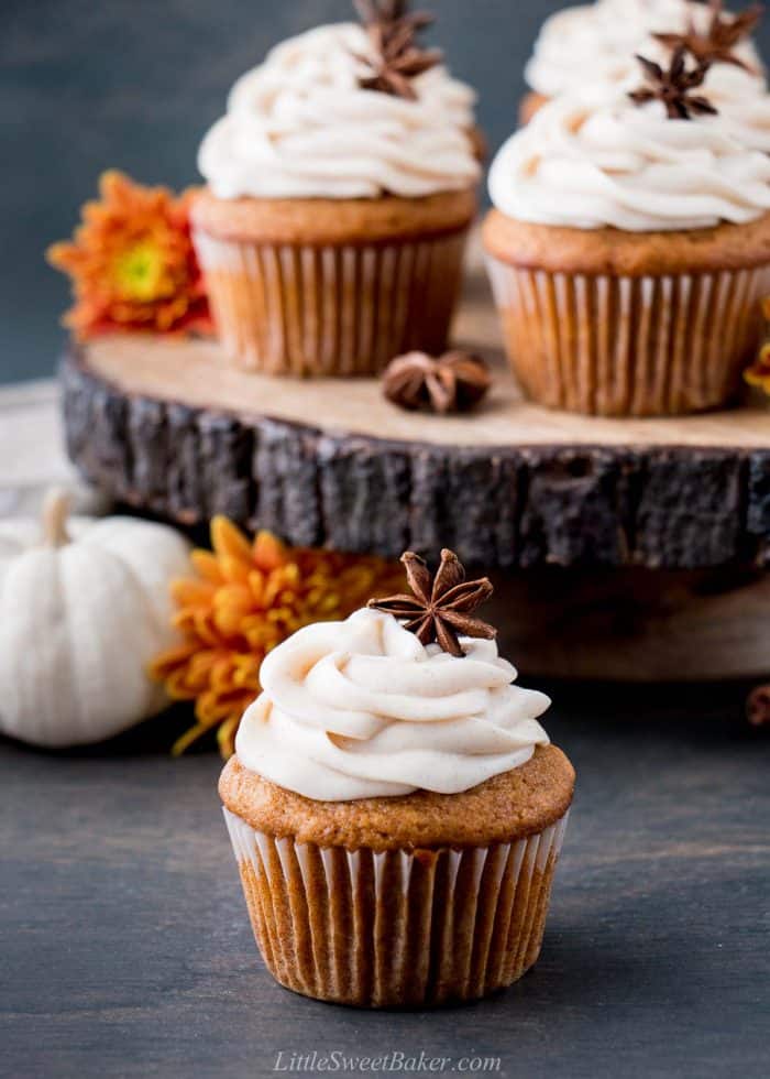 A pumpkin cupcake infront of a wooden cake stand with pumpkin cupcakes.