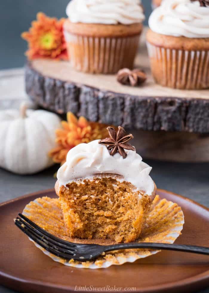 A pumpkin cupcake cut in half on a wooden plate with a fork.