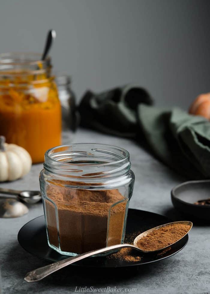 A jar of pumpkin pie spice mix on a black plate with a spoon.