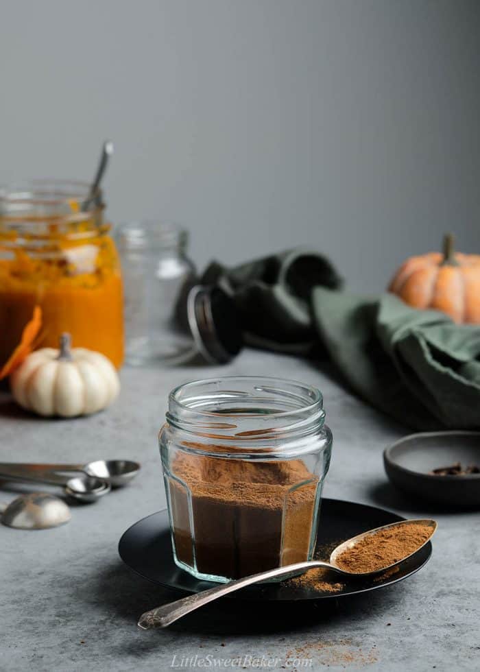 A open jar of pumpkin pie spice on a black plate with a spoonful.