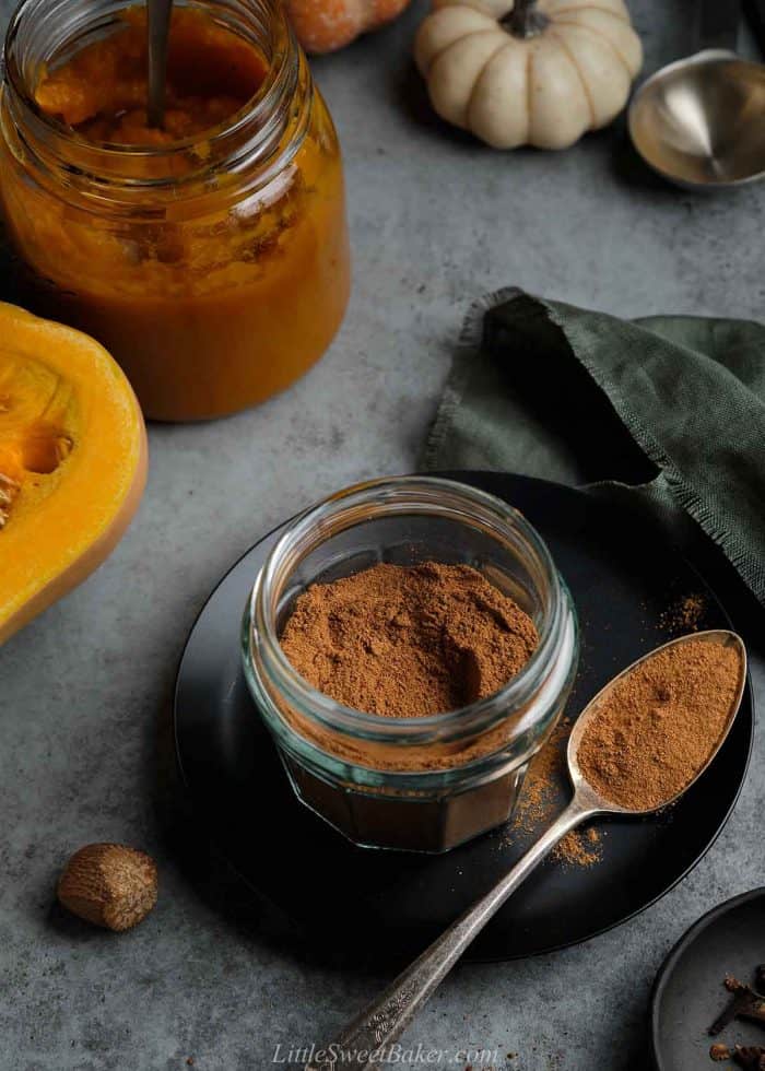 A open jar of homemade pumpkin pie spice mix on a black plate.