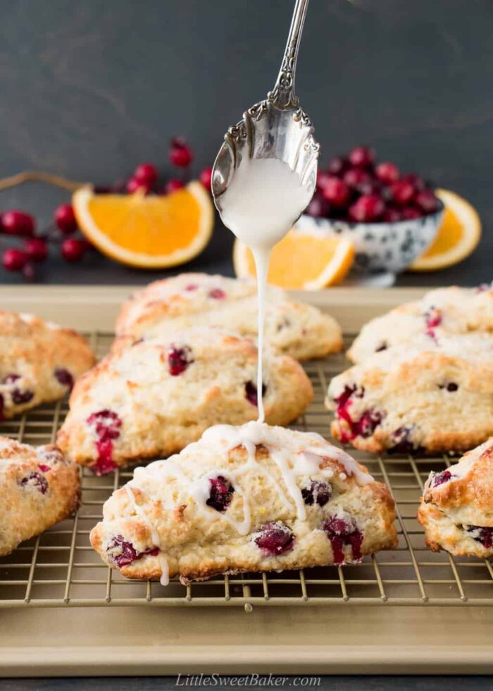 Cranberry orange scones on a cooling rack being drizzled with glaze.
