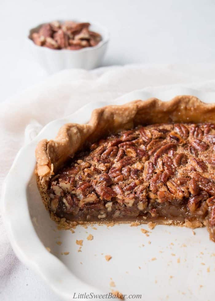 A pecan pie in a white pie plate with a quarter of the pie missing.