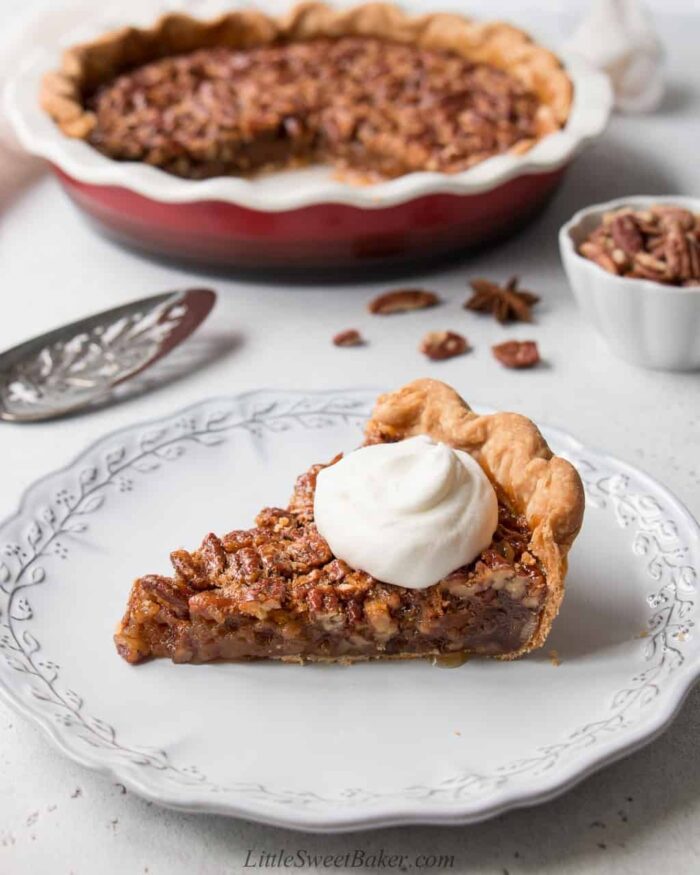 A slice of pecan pie topped with whipped cream in a light grey plate.