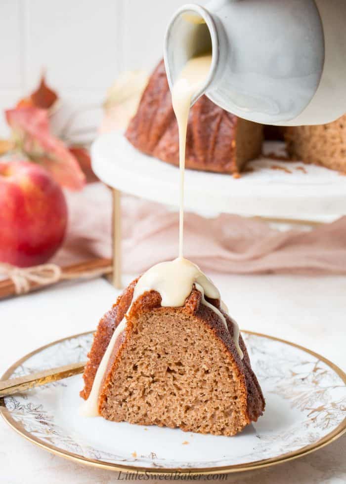 Custard sauce being poured over a slice of apple cider cake.