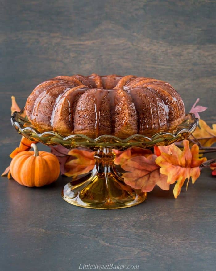 A pumpkin bundt cake topped with caramel and a vintage cake stand.