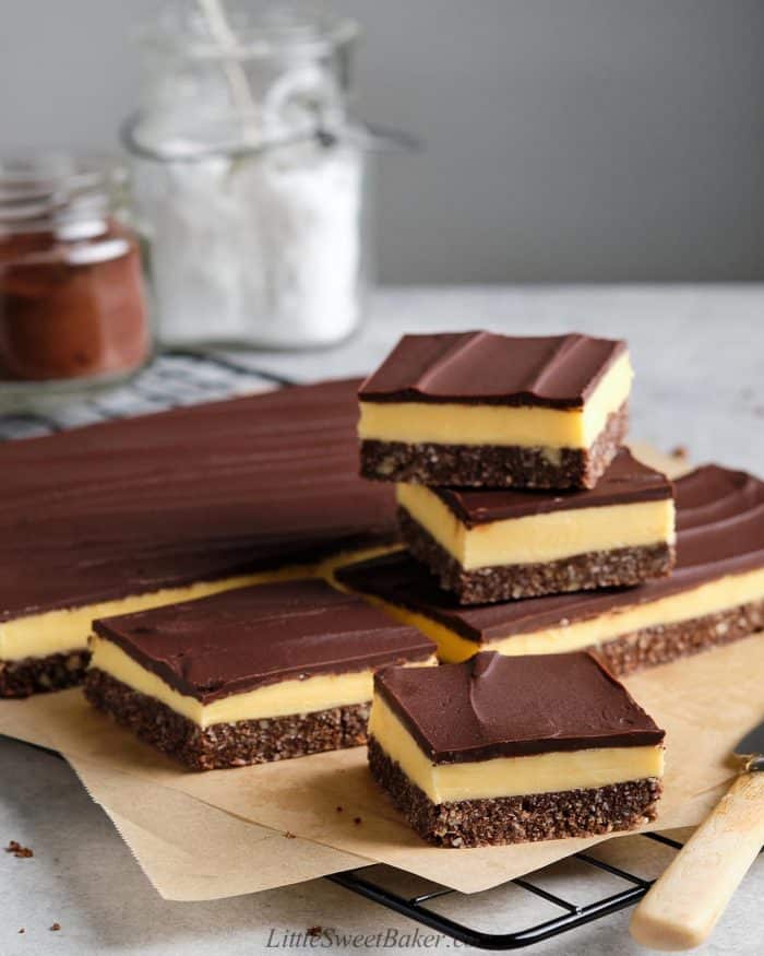 A slab of Nanaimo bars partially cut on parchment paper.