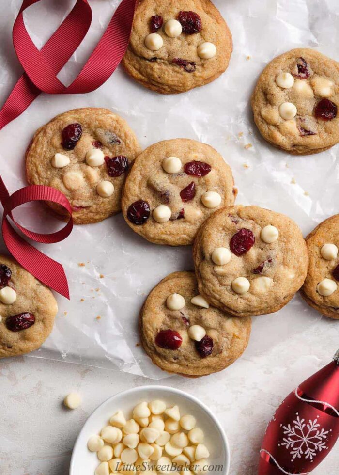 White chocolate cranberry cookies scattered on a surface with red ribbon and ornament.