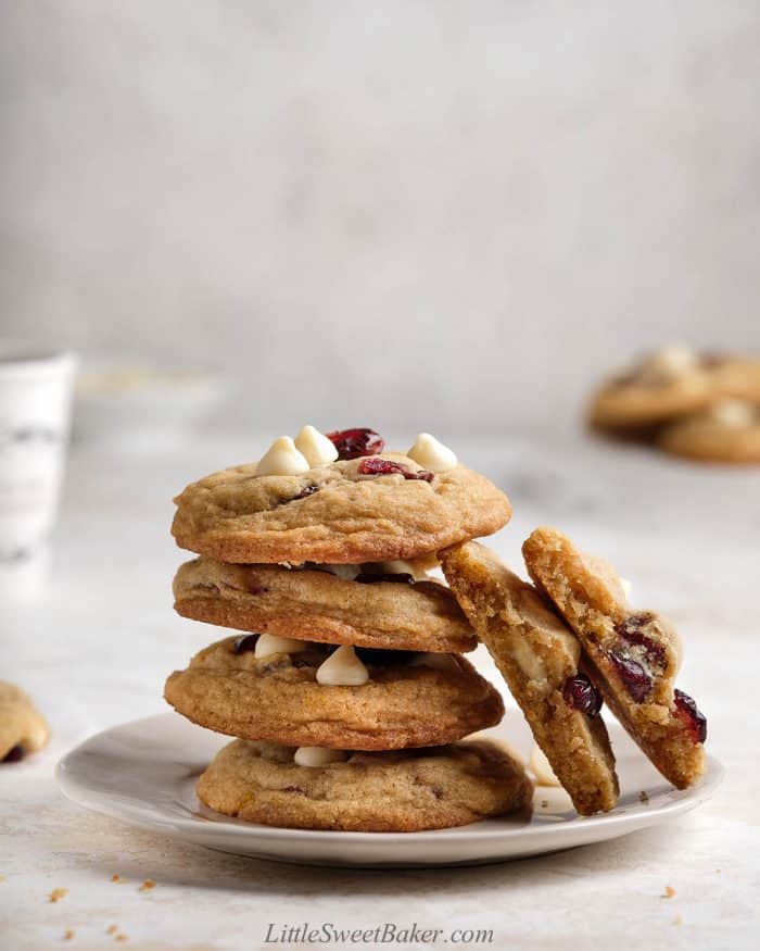 A stack of white chocolate cranberry cookies on a plate with one cookie broken in half.