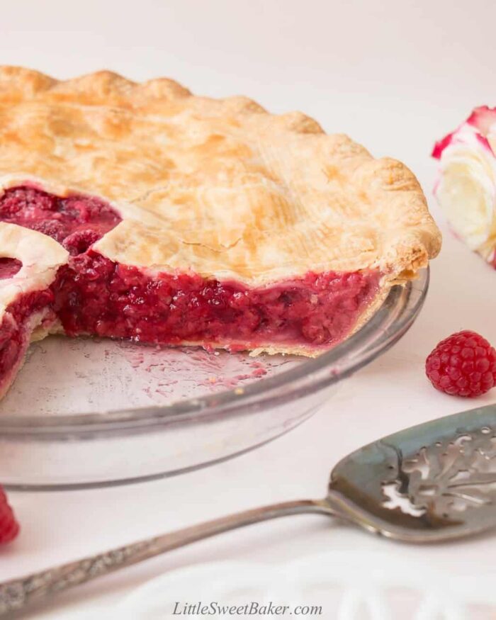 A raspberry pie in a glass pie plate with a section cut out.
