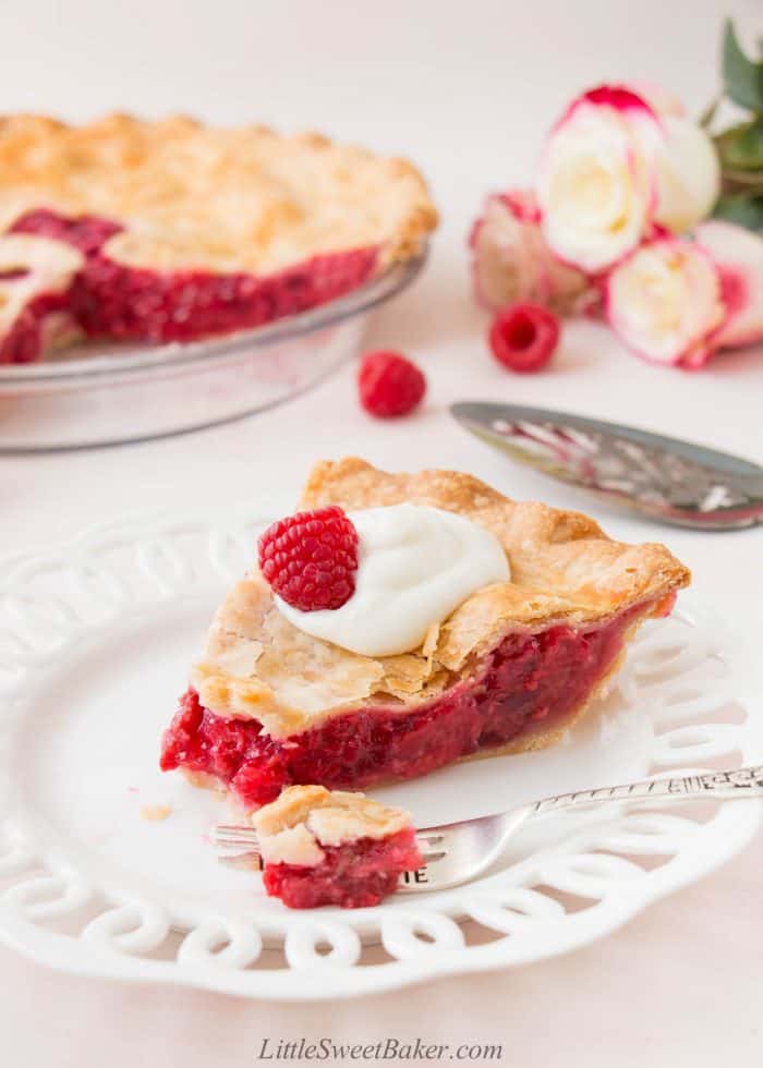 A slice of raspberry pie topped with whipped cream on a white plate.