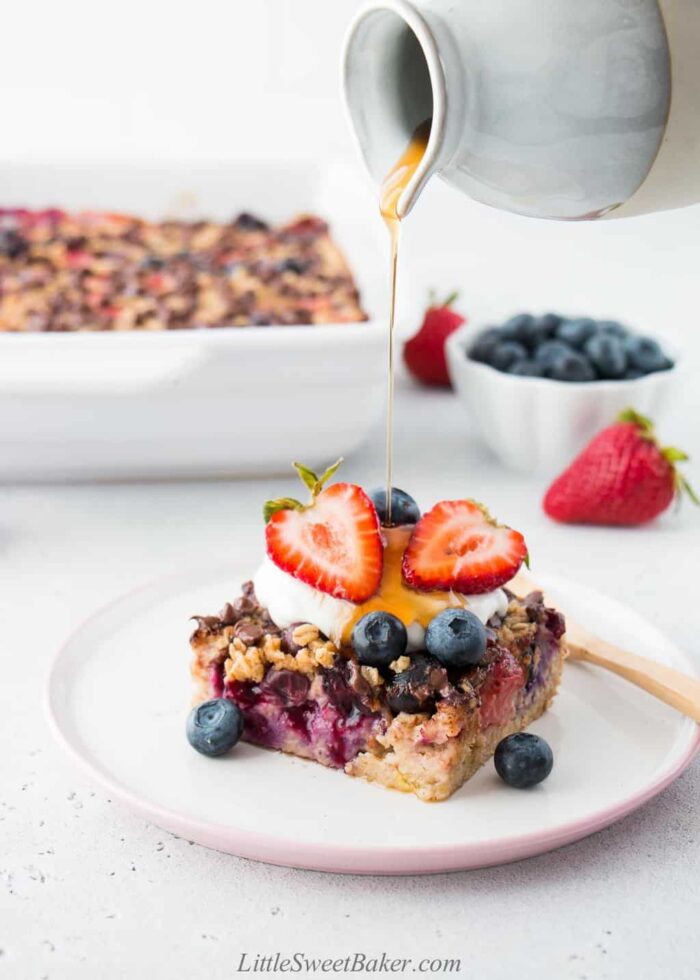 Maple syrup being poured on top of baked oatmeal topped with yogurt and berries.