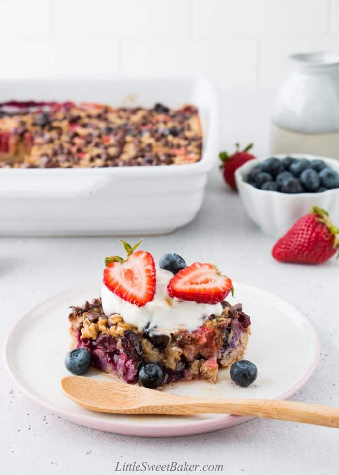 Baked oatmeal topped with yogurt and berries on a plate with a wooden spoon.